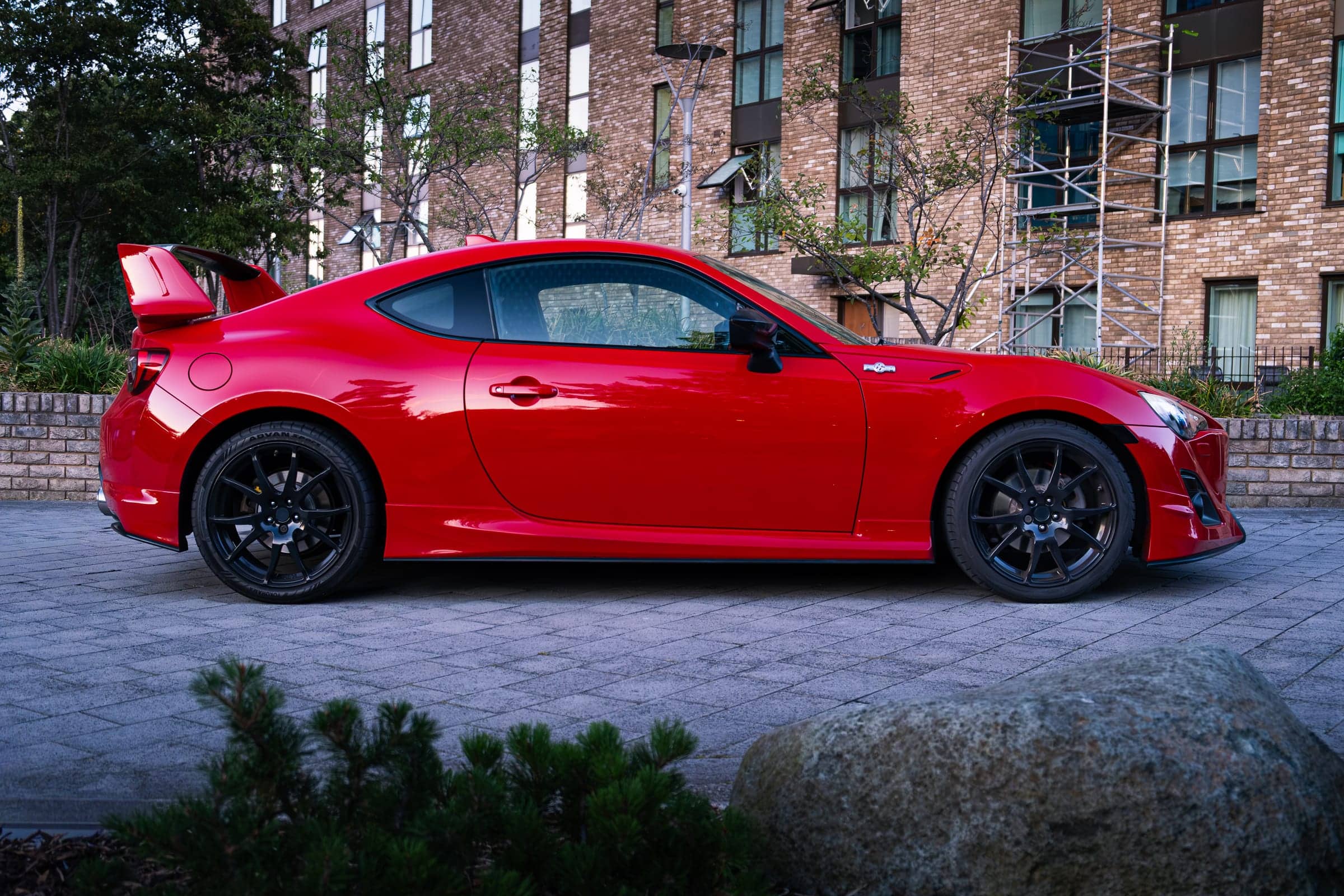 Red widebody Toyota GT86 Aero side profile outside an apartment building