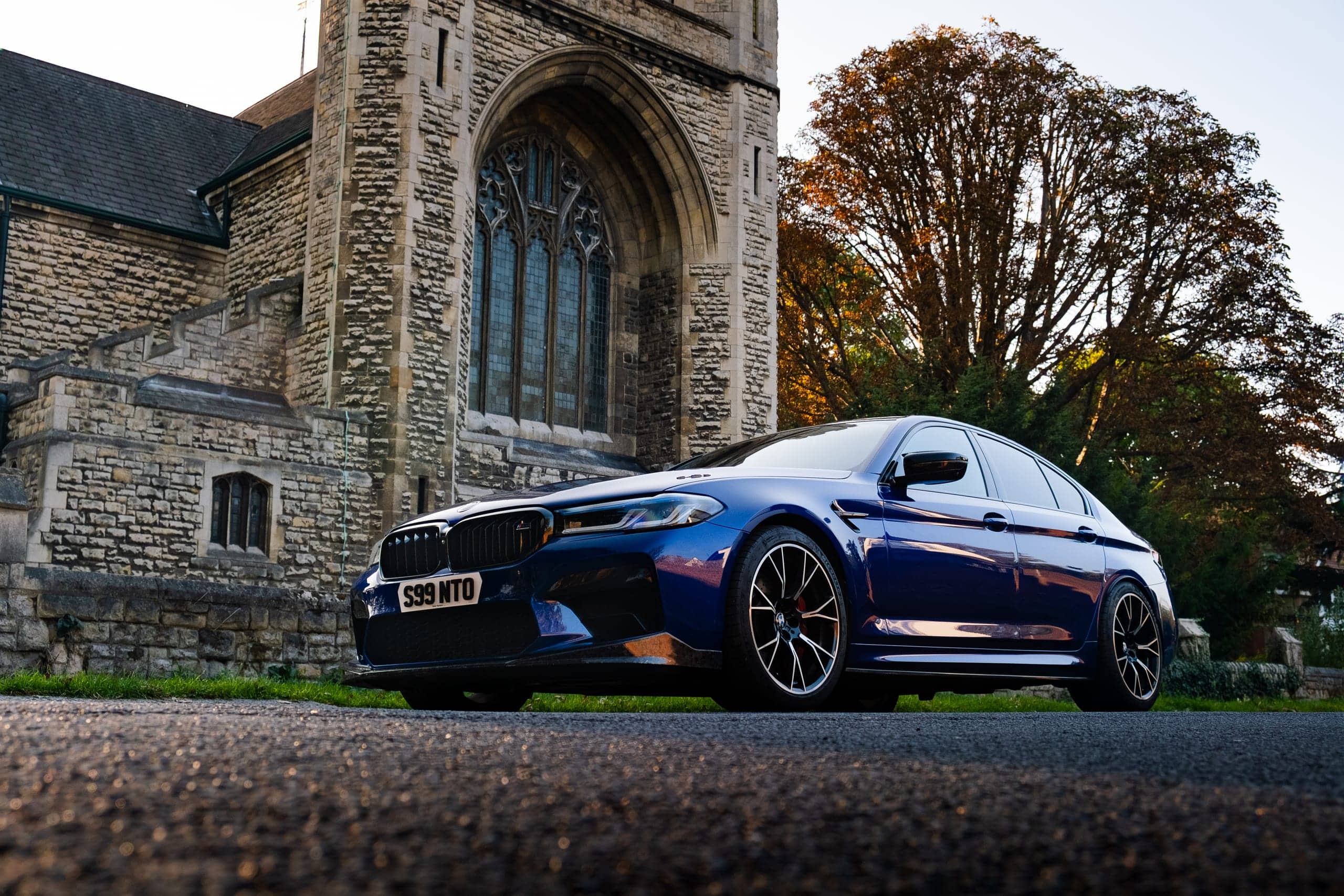BMW M5 Competition, low front three-quarter view outside a stone church at golden hour