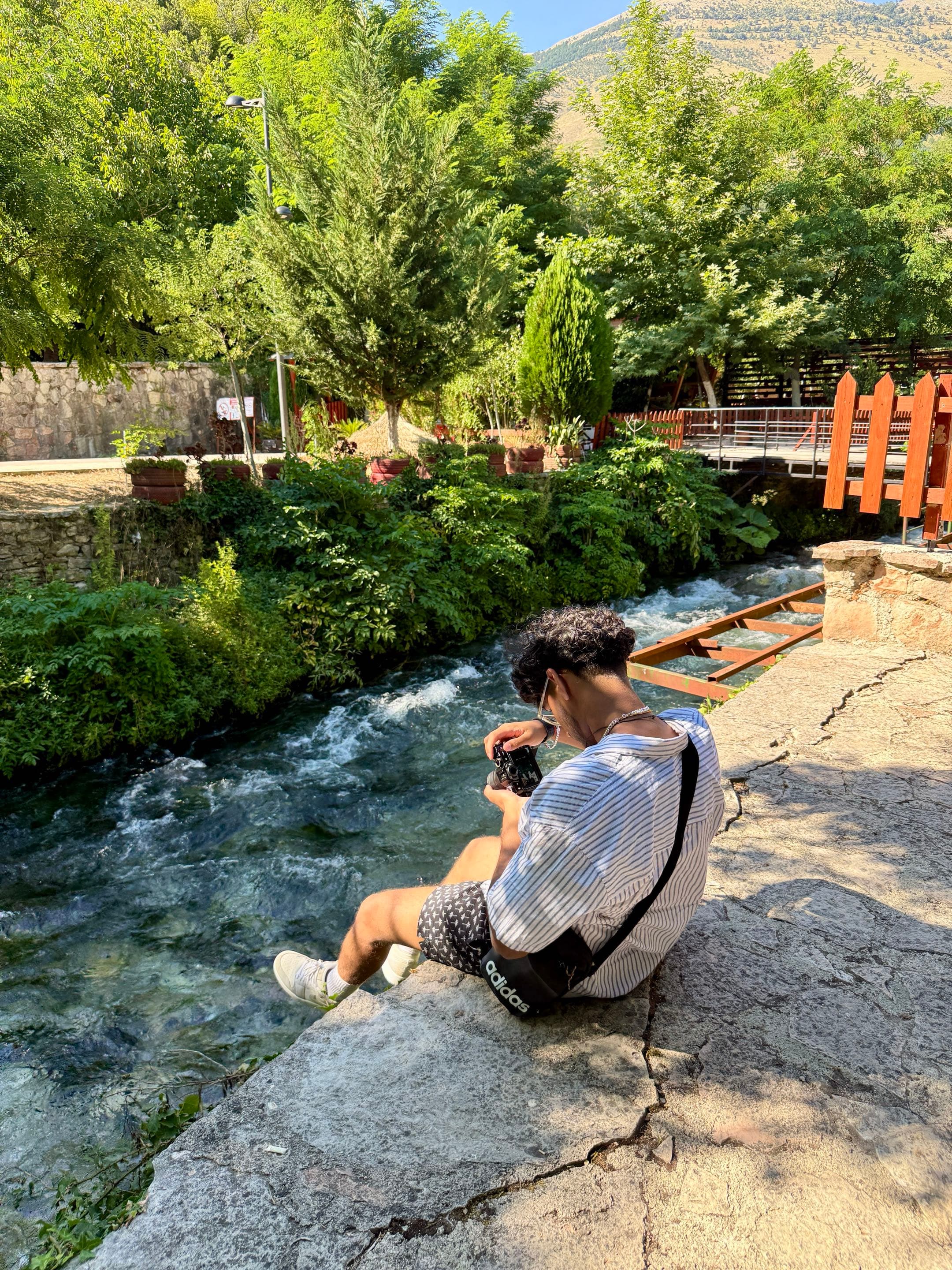 Krish crouched beside a stream, camera in hand